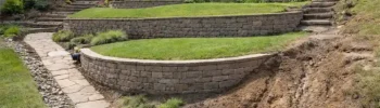 Sloped suburban backyard showing retaining walls, drainage channels, and areas of soil erosion.