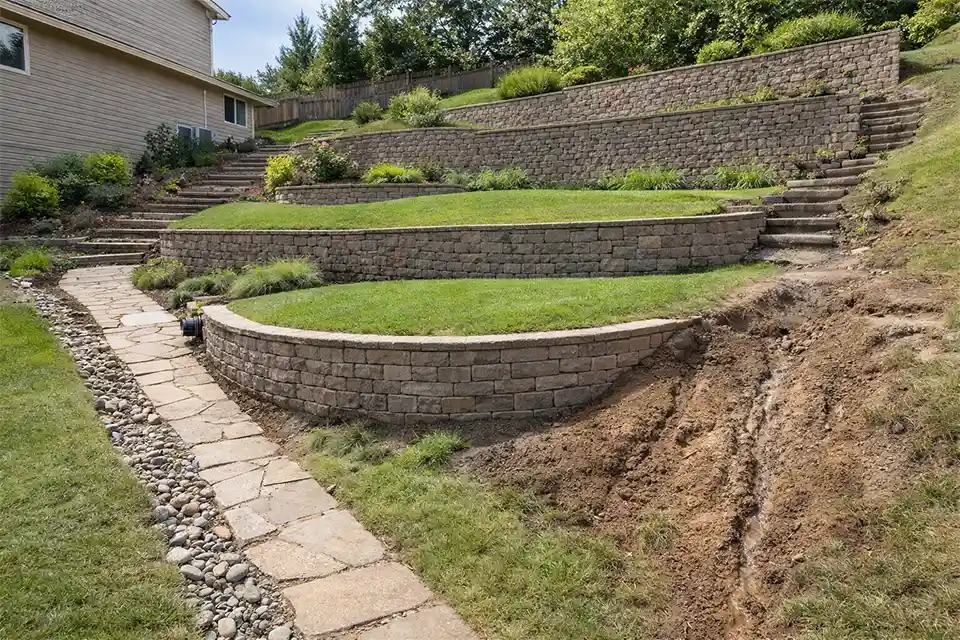 Sloped suburban backyard showing retaining walls, drainage channels, and areas of soil erosion.