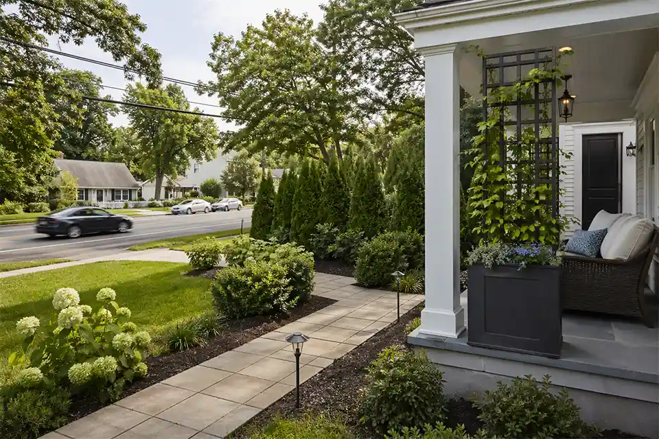 Front yard privacy design using layered shrubs and a planter with trellis to block a busy road view without a fence.