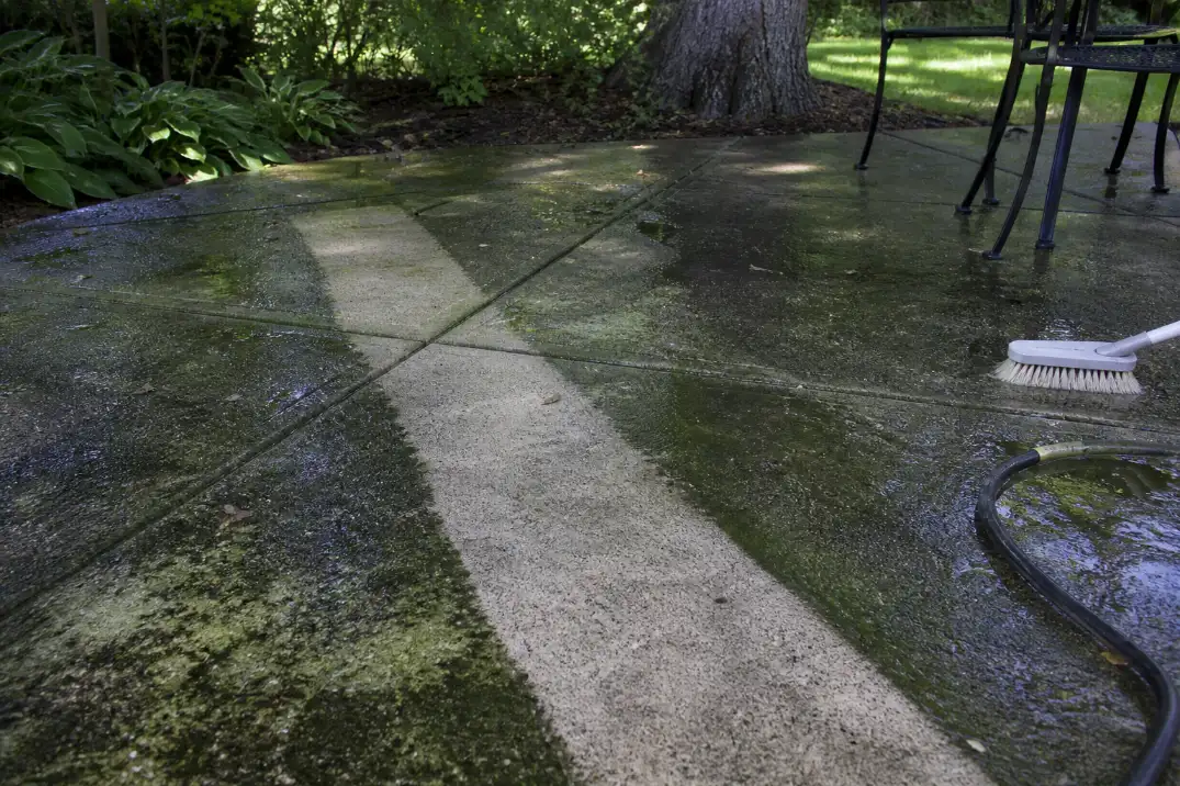 Shaded concrete patio with green algae film and a cleaned test strip showing why algae cleaner is the first fix for a slippery patio.